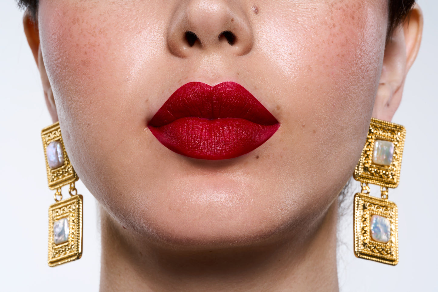 Close-up of a woman's face with red lipstick and gold earrings on a white background
